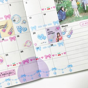 K&ouml;nnte beinhalten: Ein Monatskalender mit einem rosa-blauen Farbschema. Der Kalender hat ein Rasterlayout mit Daten und Wochentagen. Es gibt Aufkleber mit Herzen, Schleifen und Kirschen. Der Kalender hat auch einen Memo-Bereich mit einem Aufkleber, auf dem "HYEIN'S BIRTHDAY" steht.