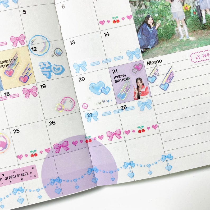 K&ouml;nnte beinhalten: Ein Monatskalender mit einem rosa-blauen Farbschema. Der Kalender hat ein Rasterlayout mit Daten und Wochentagen. Es gibt Aufkleber mit Herzen, Schleifen und Kirschen. Der Kalender hat auch einen Memo-Bereich mit einem Aufkleber, auf dem "HYEIN'S BIRTHDAY" steht.