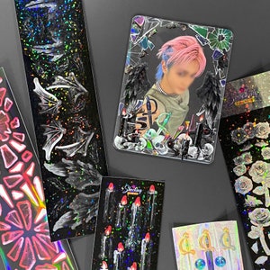 May include: A set of 10 holographic stickers featuring a variety of designs, including a person with wings, candles, and a skull. The stickers are on a black background and have a glittery finish.