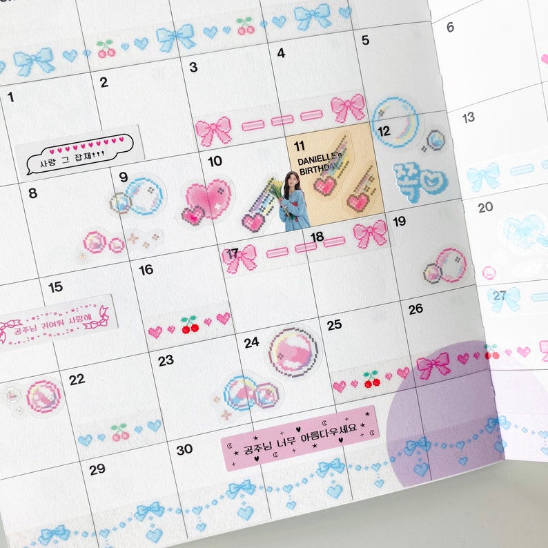 K&ouml;nnte beinhalten: Ein rosa und blauer Kalender mit Aufklebern mit Schleifen, Herzen, Kirschen und einem Comic-Charakter. Der Kalender hat den Text "DANIELLE BIRTHDAY" und "공주님 너무 아름다우세요*" geschrieben.