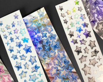 May include: Four sheets of iridescent star stickers. The stickers are on a white background and have a holographic finish. The stickers are in different colors, including blue, green, and purple.