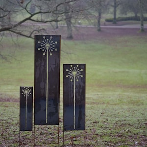 May include: Three metal garden sculptures in the shape of stylized flowers. The sculptures are different sizes and are arranged in a row on a grassy lawn.