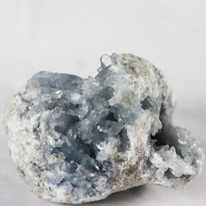 May include: A large, rough, gray rock with a cluster of light blue crystals growing from the inside. The crystals are sharp and pointed, and they create a beautiful contrast against the gray rock.