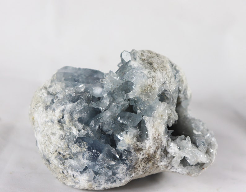 May include: A large, rough, gray rock with a cluster of light blue crystals growing from the inside. The crystals are sharp and pointed, and they create a beautiful contrast against the gray rock.