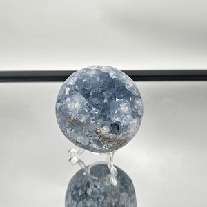 May include: A blue celestite crystal sphere on a clear stand. The sphere is made of many small crystals that are clustered together.