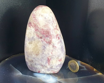 May include: A large, polished stone sculpture with a rounded top and a smooth, egg-like shape. The stone features a mix of colors, including white, pink, and purple, with a swirling pattern. A coin is next to the stone for size comparison.