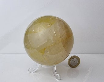 Puede incluir: Una gran esfera de citrino amarillo claro sobre un soporte de plástico transparente. La esfera tiene un diámetro de aproximadamente 5 cm.