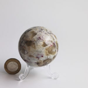May include: A white, brown, and pink crystal sphere on a clear plastic stand. The sphere is about the size of a golf ball.