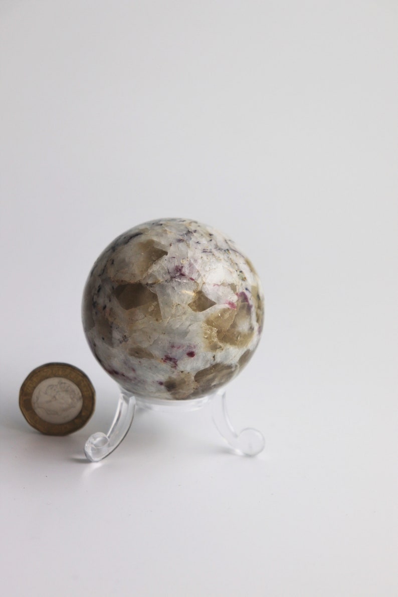 May include: A white, brown, and pink crystal sphere on a clear plastic stand. The sphere is about the size of a golf ball.