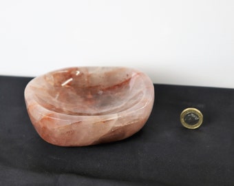 Könnte beinhalten: Eine hellrosa und rote Kristallschale mit einer glatten, abgerundeten Form. Die Schale ist aus natürlichem Quarz gefertigt und hat ein einzigartiges, organisches Aussehen.