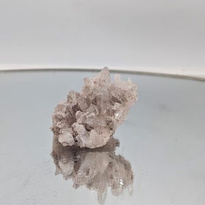 Op de afbeelding: Een cluster van kleine, heldere kwartskristallen met een licht roze tint. De kristallen zijn in een natuurlijke formatie geclusterd, waardoor een unieke en interessante vorm ontstaat.