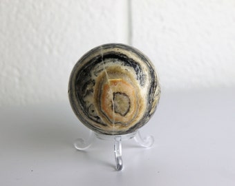 May include: A black and white banded sphere with a light orange center, displayed on a clear plastic stand.