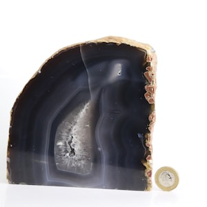May include: A large, dark grey agate geode bookend with a white and grey banded pattern. A British coin is placed next to the geode for scale.