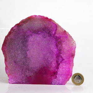 May include: A large, pink agate geode with a natural, irregular shape. The geode is approximately 15 cm tall and 13 cm wide. It has a smooth, polished surface and a variety of pink and white hues.
