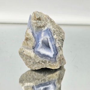 Könnte beinhalten: Ein rauer, grauer Stein mit einem blauen und weißen Achat-Geoden im Inneren. Der Geode hat eine dreieckige Öffnung.
