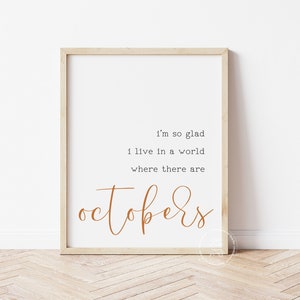 May include: A framed print with a white background and brown text that reads "I'm so glad I live in a world where there are Octobers".