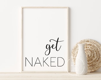 May include: A framed white print with the words "get NAKED" in black script and block letters. A white vase and a woven circular placemat are to the right of the print. The frame is light wood.