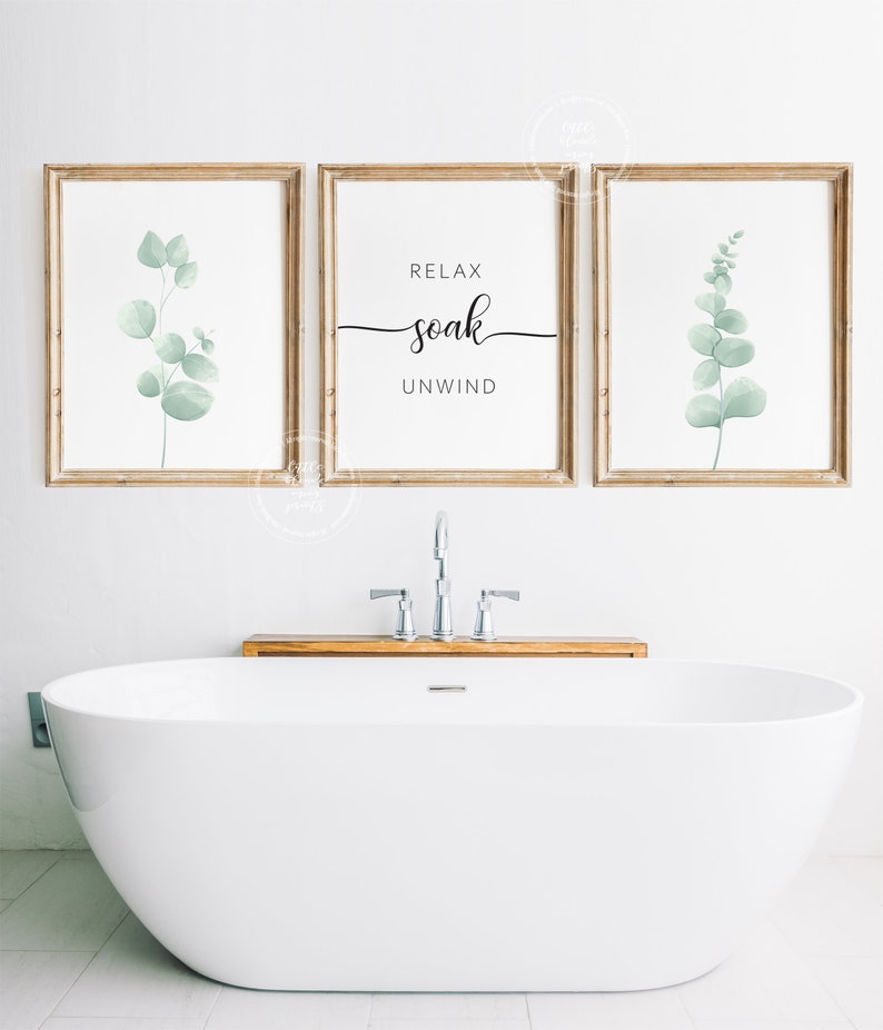 May include: Three framed prints with a white background and wooden frames. The center print has the text "Relax soak unwind" in black cursive font. The left and right prints feature a watercolor illustration of a green eucalyptus branch.