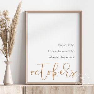 May include: A framed print with a white background and brown text that reads "I'm so glad I live in a world where there are Octobers".