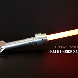 May include: A silver lightsaber with a red blade. The lightsaber is made of metal and has a textured handle. The text "THEPACHSTORE BATTLE BRICK SABER" is visible in the image.