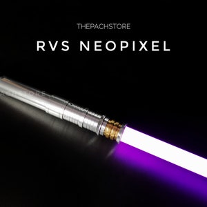 Op de afbeelding: Een zilveren lightsaber met een paarse blade. De lightsaber heeft een gouden accent in de buurt van de blade en de tekst "THEPACHSTORE" en "RVS NEOPIXEL" is zichtbaar.