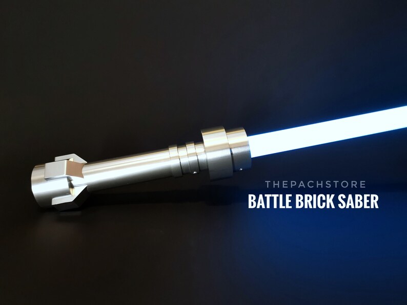 May include: A silver lightsaber with a blue blade. The lightsaber is made of metal and has a textured surface. The text "THEPACHSTORE BATTLE BRICK SABER" is visible in the image.