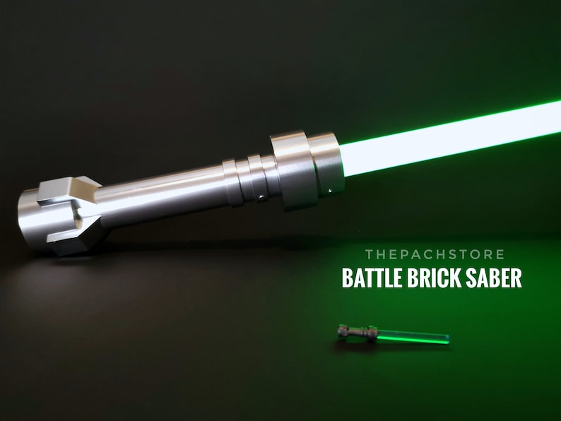 May include: A silver lightsaber hilt with a green blade. The hilt is made of metal and has a textured surface. The blade is about 2 feet long and is glowing brightly. The text "THEPACHSTORE BATTLE BRICK SABER" is visible below the lightsaber.