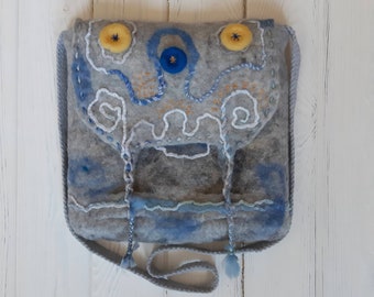 May include: A gray felt crossbody bag with blue and yellow embroidery. The bag has a flap with a blue button and two yellow buttons. The strap is gray and has tassels.