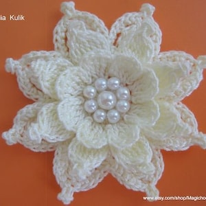 May include: A white crocheted flower with a pearl center. The flower is made with a delicate crochet stitch and has a layered design.