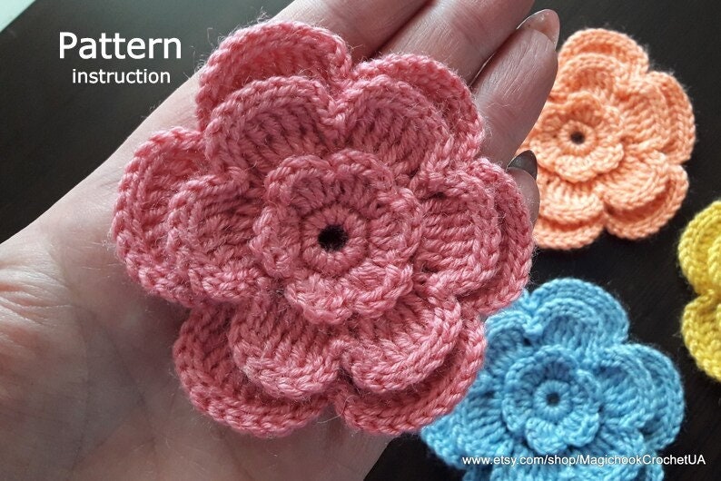 May include: A crochet pattern instruction for making a flower. The image shows three crocheted flowers in pink, blue, and orange.