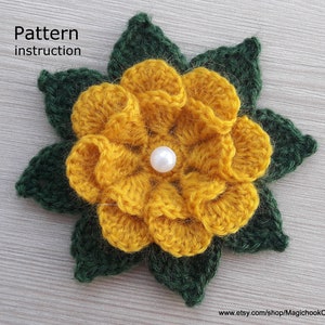 Puede incluir: Una flor amarilla tejida a crochet con hojas verdes y una perla blanca en el centro. La flor está hecha con un punto texturizado y tiene un aspecto arrugado. Las hojas son de un verde más oscuro y tienen una forma puntiaguda. La flor es un artículo artesanal hecho a mano.