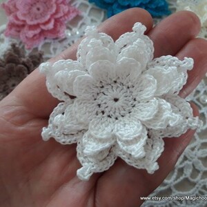 May include: A white crocheted flower with multiple layers of petals. The flower is delicate and intricate, with a small center.