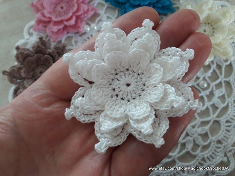 May include: A white crocheted flower with multiple layers of petals. The flower is delicate and intricate, with a small center.
