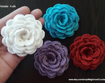 May include: Four crocheted flowers in white, turquoise, purple, and red. The flowers are arranged on a dark surface.