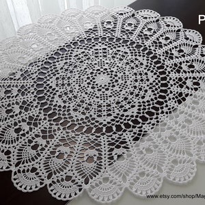 May include: White crochet doily with a delicate, intricate pattern. The doily is circular and has a scalloped edge. The pattern is reminiscent of a flower or a star.
