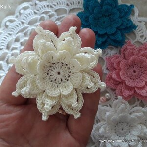 May include: Three crocheted flowers in different colors: white, pink, and teal. The flowers are made with a delicate, lacy stitch and have a layered, ruffled appearance.
