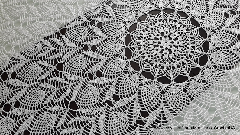 May include: White, handmade crochet doily with a detailed floral and geometric design. The doily features a central circular motif surrounded by intricate patterns. The delicate lace-like texture is visible against a dark background.