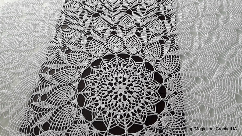 May include: White, intricately crocheted doily with a central circular design and repeating patterns. The delicate lace-like texture is visible throughout the piece, creating a detailed and elegant appearance. The doily is likely handmade.