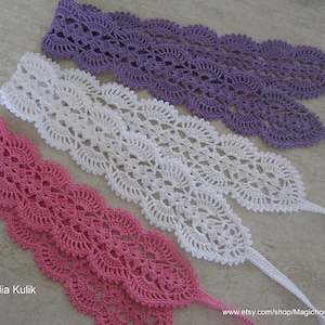 May include: Three crocheted lace trims in pink, white, and purple. Each trim has a scalloped edge and a delicate floral pattern.
