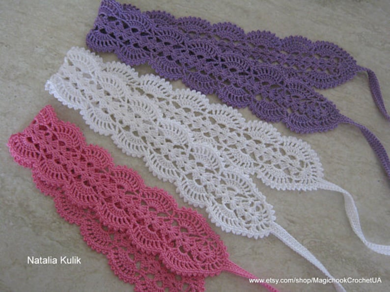 May include: Three crocheted lace trims in pink, white, and purple. Each trim has a scalloped edge and a delicate floral pattern.