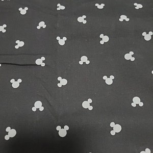 May include: Black fabric with a repeating pattern of white Mickey Mouse head silhouettes. The fabric has a smooth texture and the Mickey Mouse heads are evenly spaced across the surface.