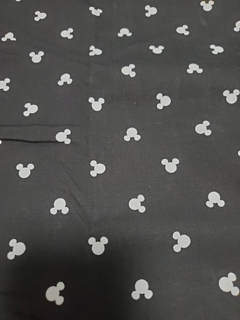 May include: Black fabric with a repeating pattern of white Mickey Mouse head silhouettes. The fabric has a smooth texture and the Mickey Mouse heads are evenly spaced across the surface.