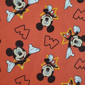 Puede incluir: Una tela roja con un patr&oacute;n repetido de Mickey Mouse en una estrella amarilla. El fondo es de color naranja s&oacute;lido.
