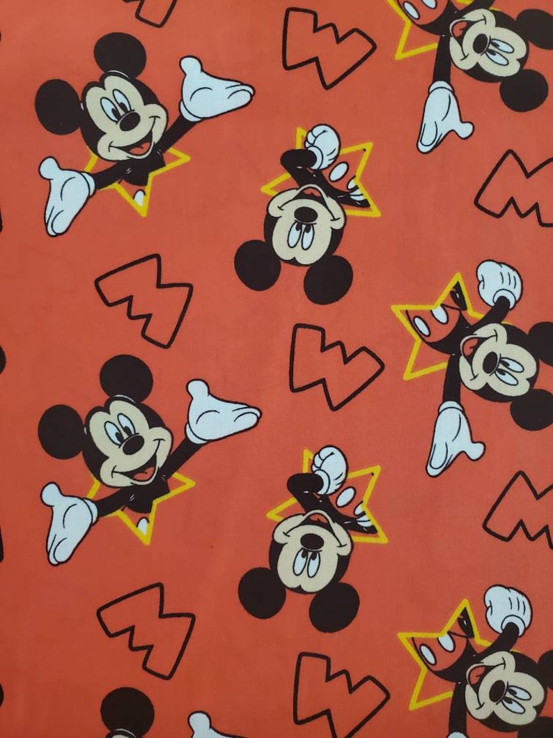 Puede incluir: Una tela roja con un patr&oacute;n repetido de Mickey Mouse en una estrella amarilla. El fondo es de color naranja s&oacute;lido.
