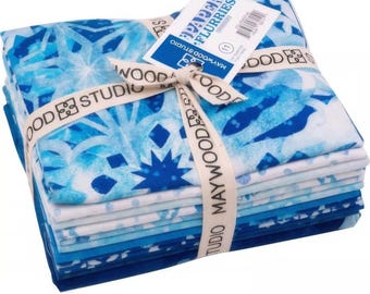 Puede incluir: Una pila de cuadrados de tela en tonos azules y blancos, atados con una cinta que dice "MAYWOOD STUDIO". La tela presenta un patrón similar a un copo de nieve. Una etiqueta dice "PAPER FLURRIES".