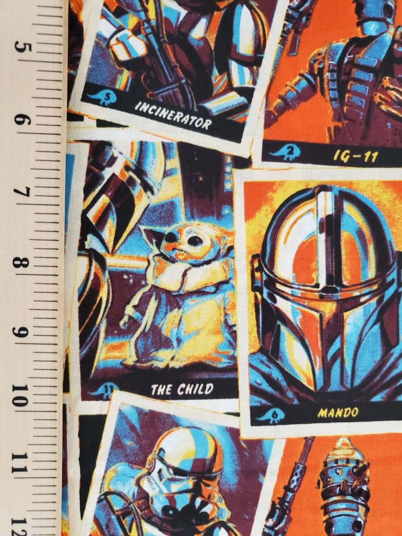 May include: A colorful fabric with a repeating pattern of trading cards featuring characters from the Star Wars universe. The cards feature images of characters like The Child, Mando, IG-11, and Incinerator. The cards have a vintage look with a white background and a yellow border.