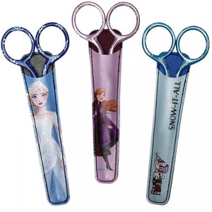 May include: Three pairs of decorative scissors with character-themed sheaths. The scissors have silver blades and patterned handles. The sheaths feature images of Elsa, Anna, and Olaf from the movie Frozen, with the text "SNOW-IT-ALL" on one.