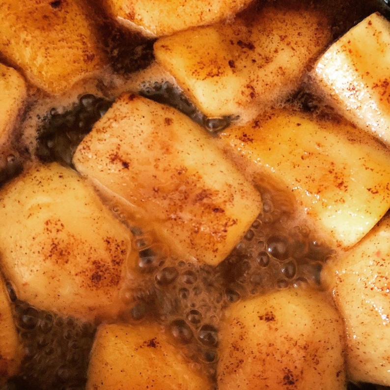 K&ouml;nnte beinhalten: Nahaufnahme eines Topfes mit &Auml;pfeln, die in einer braunen Fl&uuml;ssigkeit k&ouml;cheln. Die &Auml;pfel sind mit einer Zimt-Zucker-Mischung &uuml;berzogen und haben eine goldbraune Farbe.