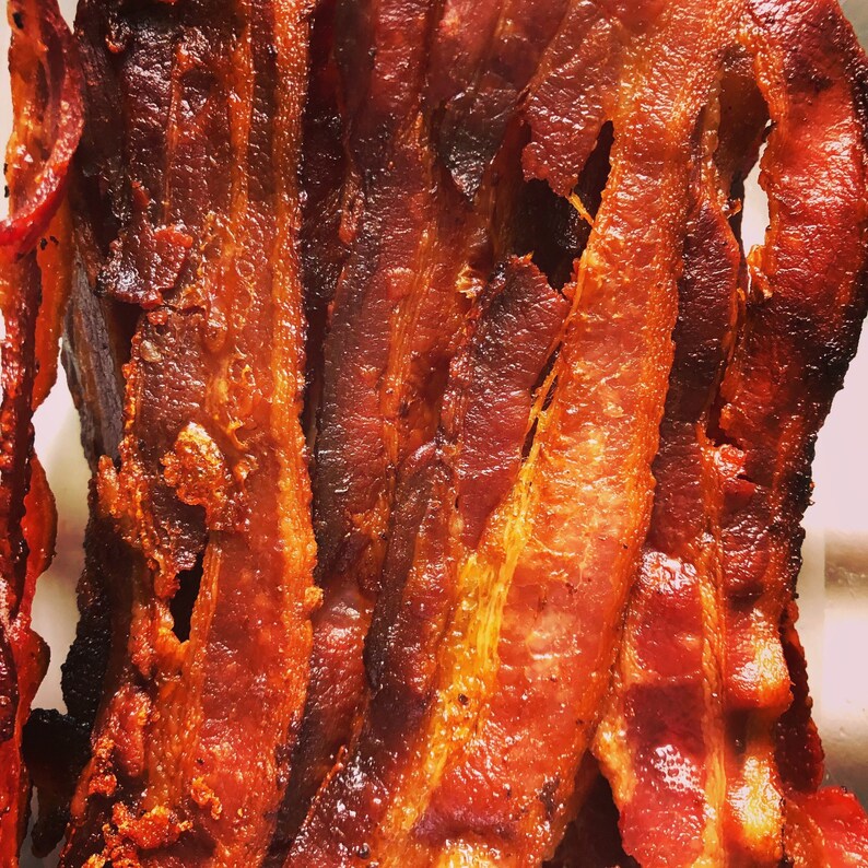 May include: Close-up of crispy bacon strips, showcasing a range of colors from deep brown to reddish-orange. The bacon appears cooked to a perfect crisp, with visible textures and rendered fat. The image highlights the savory appeal of the breakfast staple.
