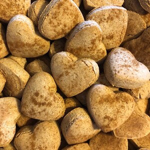 K&ouml;nnte beinhalten: Ein Nahaufnahmebild eines Stapels herzf&ouml;rmiger Kekse. Die Kekse sind hellbraun und haben eine leicht raue Textur. Sie scheinen hausgemacht zu sein und haben ein rustikales Aussehen.